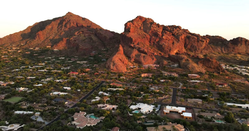 Aerial view of a residential area nestled at the base of rugged red rock mountains in Phoenix, Arizona, illuminated by the warm light of the setting sun