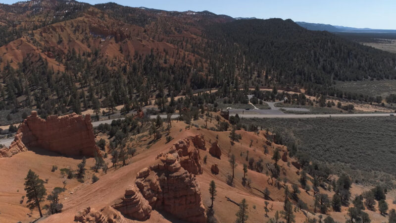 Rugged desert landscape of Red Rock Canyon's near Las Vegas, featuring striking red rock formations, scattered pine trees, and winding roads cutting through the scenic terrain