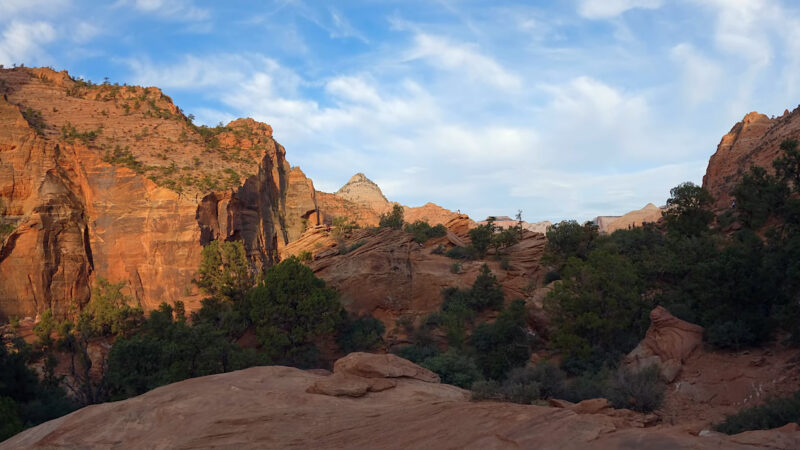 stunning view of the Canyon Overlook Trail, showcasing majestic red rock formations and vibrant green vegetation under a clear blue sky with scattered clouds.